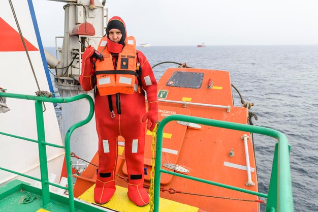 Marinero con traje de inmersión en la estación de reunión Abandonar el taladro del barco Barco de carga de caída libre