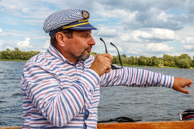 Marinheiro em um boné em um barco a vela contra o céu e a água