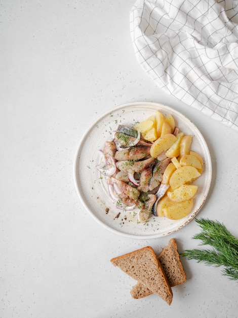 Marinierter Heringsfisch mit Kartoffelscheiben und roten Zwiebeln mit Roggenbrot auf dem weißen Tisch