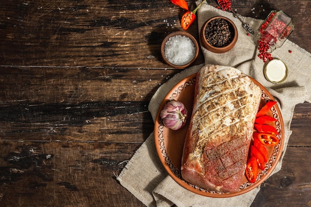 Marinierter Schweinerücken. Ein rohes Stück Fleisch zum Zubereiten festlicher Speisen. Peperoni, Gewürze, rustikaler Stil. Trendiges hartes Licht, dunkler Schatten. Alter hölzerner Hintergrund, Draufsicht