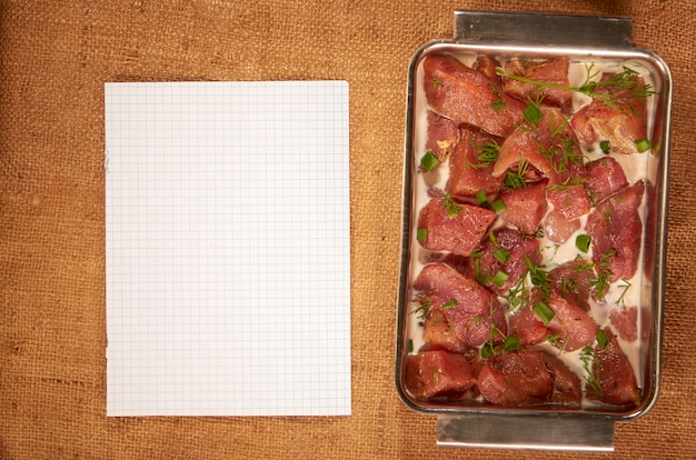 Mariniertes fleisch in milch und gemüse in einer tiefen stahlplatte auf einem hausgemachten tuch mit einem sauberen blatt papier