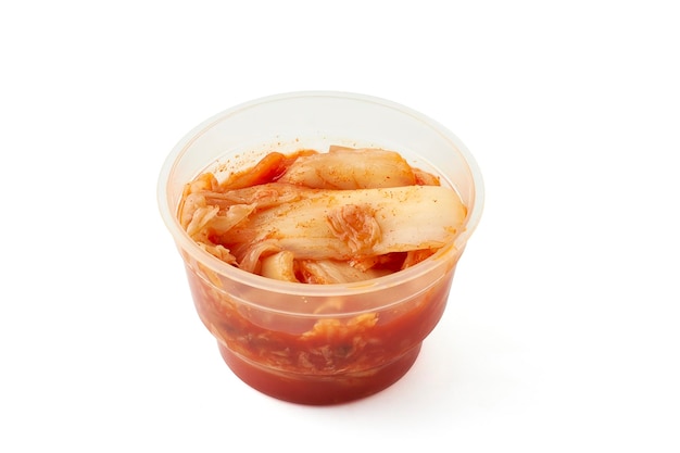 Mariniertes Kimchi mit Gemüse wie Salatkarotten in einem kleinen Plastikbecher isoliert auf weißem Hintergrund Kimchi ist ein traditionelles Gericht der koreanischen Küche. Es wird oft als Beilage gegessen