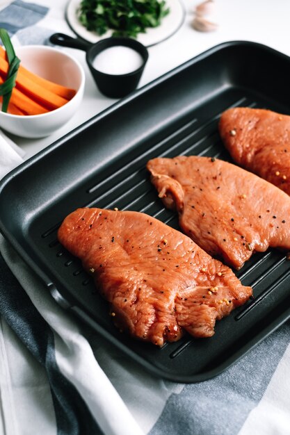 Mariniertes Putensteak mit Gewürzen in einer schwarzen Grillpfanne auf dem Tisch.