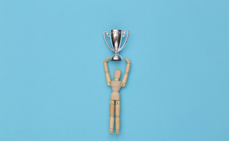 Marioneta de madera feliz sosteniendo una copa de campeonato de plata sobre un fondo azul.