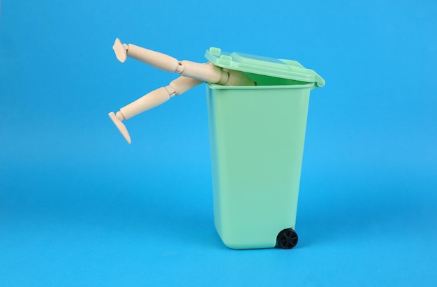 Marioneta de madera hurga en un bote de basura sobre fondo azul Concepto de pobreza