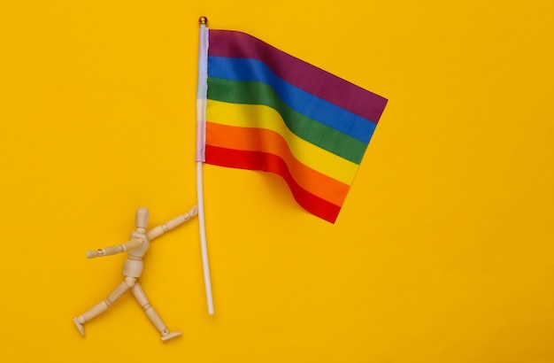 Marioneta de madera que sostiene la bandera del arco iris LGBT sobre fondo amarillo. Tolerancia, libertad, desfile gay