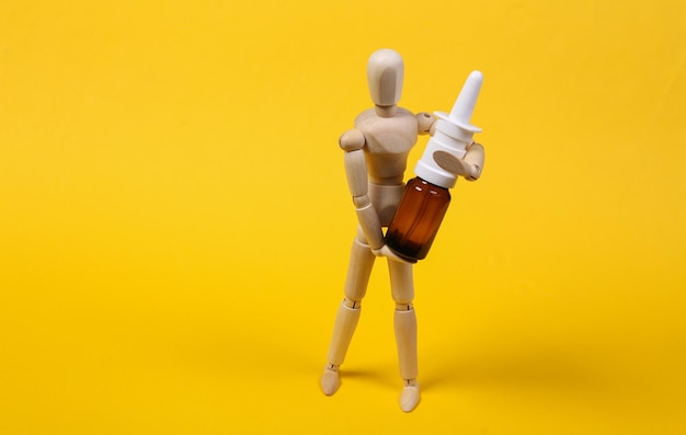 Una marioneta de madera sostiene un aerosol nasal sobre fondo amarillo. concepto de medicina