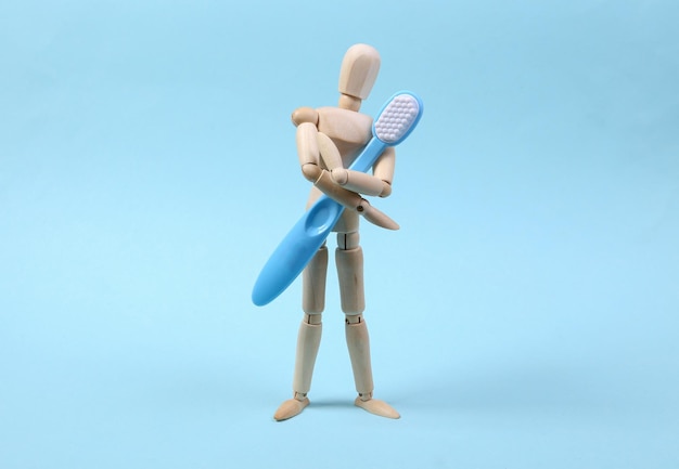 La marioneta de madera sostiene un cepillo de dientes sobre un fondo azul. Cuidado dental
