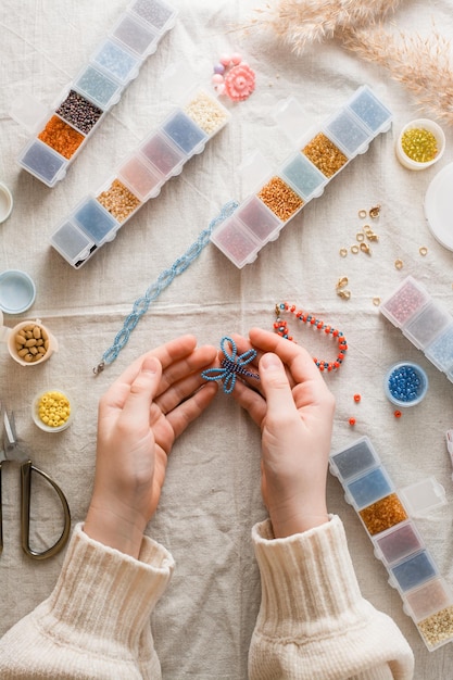 Una mariposa con cuentas en manos de una niña y artículos para trabajar con cuentas en la mesa Desarrollo de habilidades creativas y habilidades motoras finas para niños Vista superior y vertical