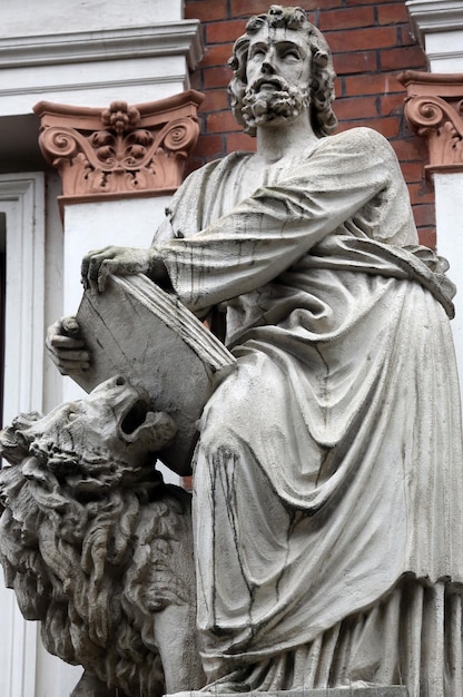 Mark el evangelista con la estatua del león contra la pared de ladrillo