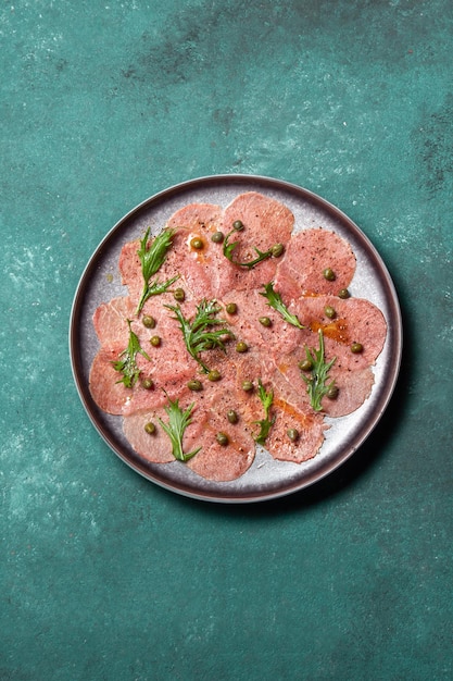 Marmoriertes Rindercarpaccio mit Arugula und Kapern auf Draufsicht des grauen Plattenblauhintergrundes