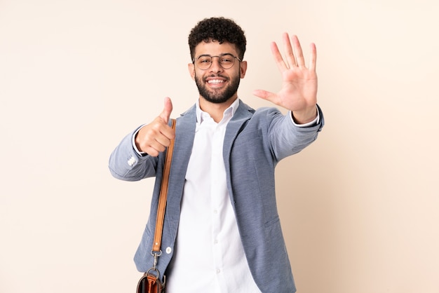 Marokkanischer Mann des jungen Geschäfts lokalisiert auf beige Wand, die sechs mit den Fingern zählt