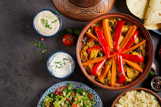 Marokkanisches Essen. Traditionelle Tajine-Gerichte, Couscous und frischer Salat auf rustikalem Holztisch. Tajine Hühnerfleisch und Gemüse. Arabische Küche. Ansicht von oben. Flach liegen