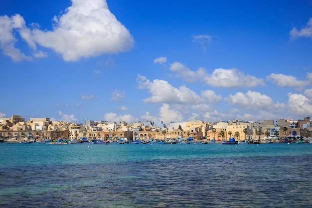 Marsaxlokk historischen Hafen voller Boote in Malta Blauer Himmel mit wenigen weißen Wolken und Dorf Hintergrund Panoramablick