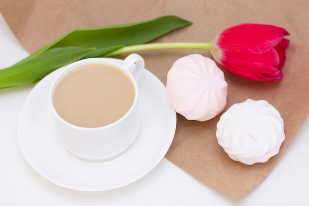 Marshmallow, chá ou café com leite e uma flor de tulipa. numa superfície clara manhã romântica de primavera. café da manhã delicado, café da manhã na cama. para o amado. surpresa.