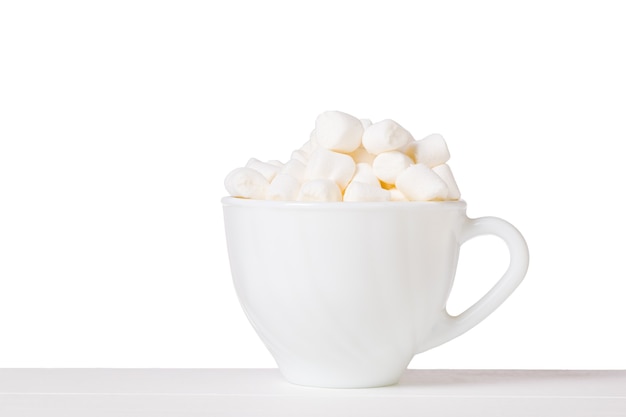 Marshmallow em uma tigela branca com uma alça sobre uma mesa branca, isolada em um fundo branco. Sobremesa deliciosa.