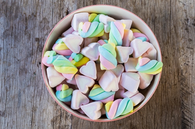 Marshmallow multicolor giro y corazón en un recipiente sobre una mesa de madera.