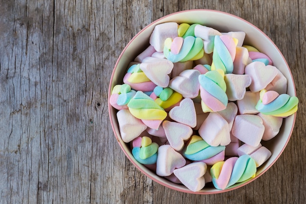 Marshmallow multicolor giro y corazón en un recipiente sobre una mesa de madera.