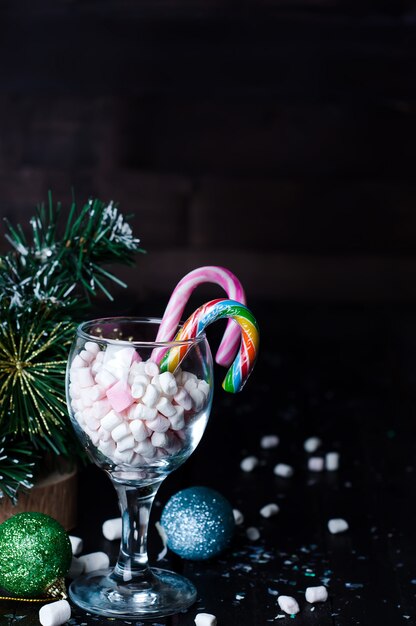 Marshmallows branco e rosa em um copo sobre a mesa de madeira escura