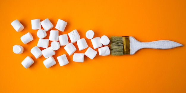 Marshmallows brancos sobre fundo amarelo com pincel de pintura. Conceito criativo de junk food insalubre. Fundo de doces de comida.