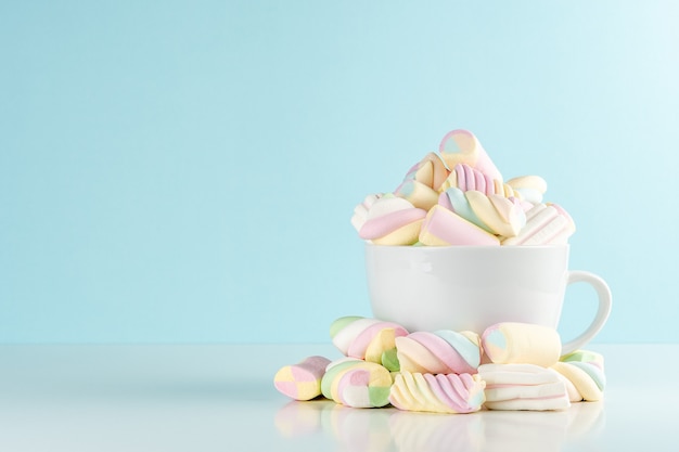 Marshmallows bunte Kaubonbons in einer Tasse auf Blau.