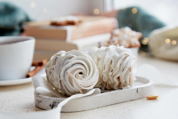 Marshmallows delicados brancos, chocolate quente, flocos de neve, biscoitos e livros em casa aconchegante em dia de neve