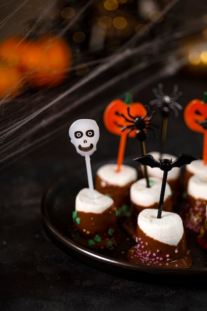 Foto marshmallows doces de halloween com cobertura de chocolate com açúcar e enfeites de halloween em um