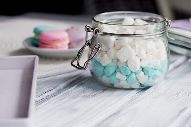 Marshmallows in weißen und blauen Pastellfarben auf heller Holzoberfläche. In einem Glas mit Klappdeckel