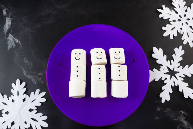 Marshmallows Schneemann auf blauem Teller und Schneeflocken an der Seite