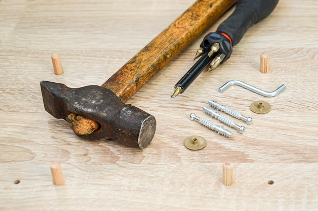 Martelo, chave de fenda e fechos em uma mesa de madeira. ferramentas e peças para montagem de móveis de gabinete sobre uma superfície de madeira a partir de uma placa de aglomerado.