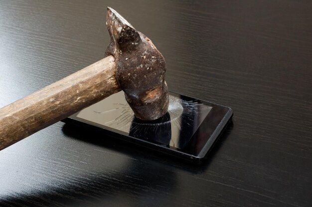 Martelo quebra o telefone na mesa de madeira