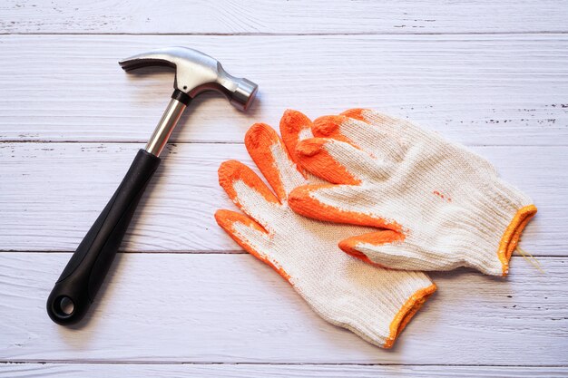 Martillo de acero y guantes de construcción de tejido naranja en madera blanca