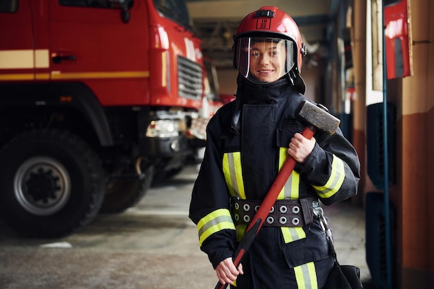 Con martillo en las manos Mujer bombero en uniforme protector de pie cerca de camión
