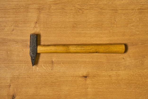 Un martillo de metal con mango de madera sobre una superficie de madera.