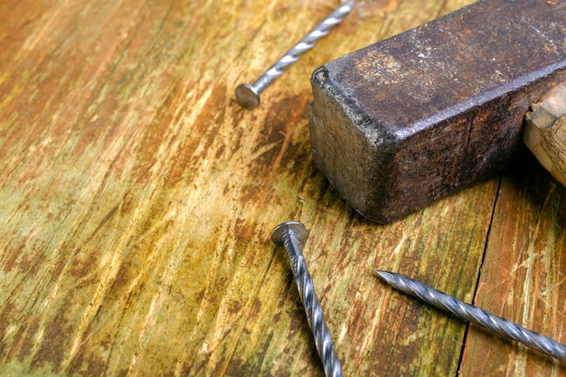 Martillo oxidado viejo y tres clavos de acero se encuentran en una mesa de madera rayada. Copiar espacio para texto.