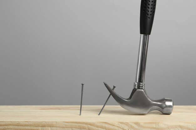 Martillo tirando de un clavo de metal de la superficie de madera contra un espacio de fondo gris para el texto