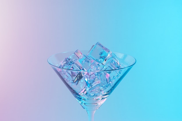 Martini-Glas mit Eiswürfeln in neonholographischen leuchtenden rosa und blauen Farben