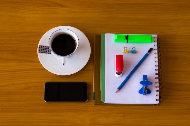 Martphone com bloco de notas e café em uma mesa de madeira.