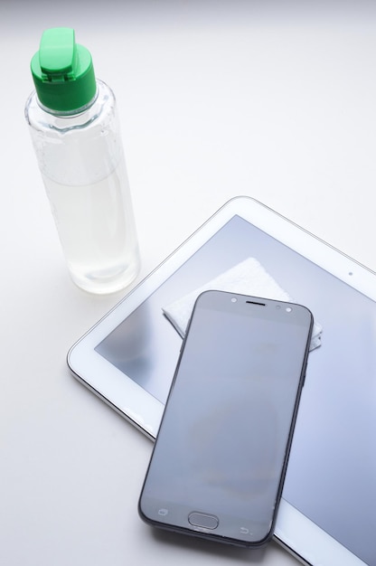 Foto martphone e tablet em um fundo branco no local com um frasco de desinfetante em gel e guardanapo. tratamento antiviral e antibacteriano de gadgets vestíveis.