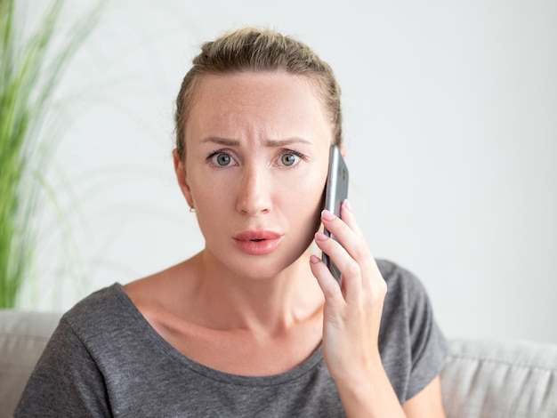 Más notícias Mulher preocupada Comunicação móvel Assuste uma senhora bonita falando smartphone sentado sofá no interior da sala de luz