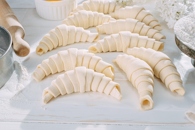 Masa de croissant enrollada y lista para hornear en una mesa de madera blanca sobre papel de hornear en el sol de la mañana