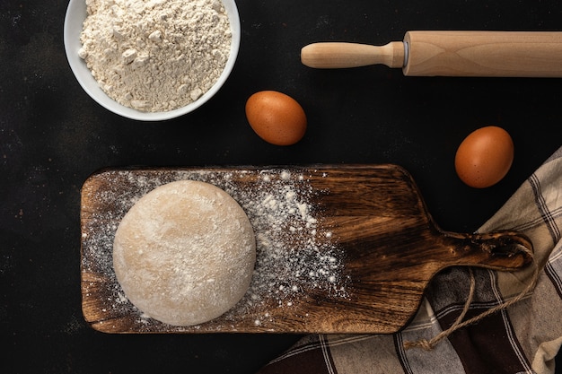 Masa cruda fresca para pan o pizza con huevos en un oscuro con espolvoreado de harina.