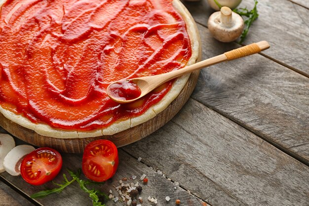 Masa cruda con salsa de tomate e ingredientes para pizza en la mesa