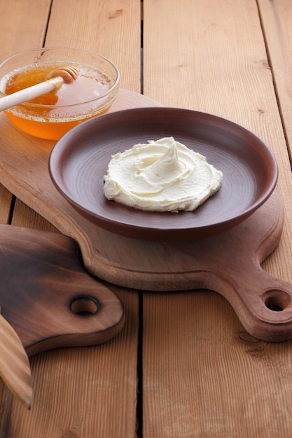 Foto masa de cuajada en un plato de arcilla sobre una tabla de madera bodegón con queso y miel sobre un fondo negro de madera primer plano