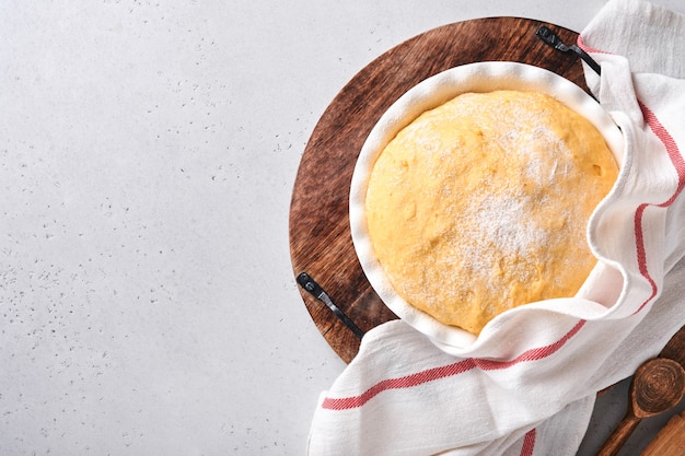 Foto masa de levadura cruda con calabaza en un tazón blanco cubierto con una toalla sobre la mesa de la cocina enharinada, idea de la receta. concepto casero para hornear pan, bollos o cinnabon o hacer masa.