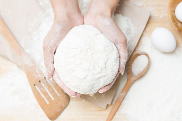 Masa de levadura cruda en tus manos sobre una mesa de cocina enharinada, la idea de una receta. El concepto de hornear en casa o hacer masa.