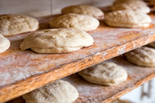 Masa de pan cruda preparada en forma de panes en estantes de madera listos para entrar al horno en una panadería