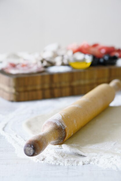 Masa y rodillo sobre la mesa blanca con ingredientes borrosos