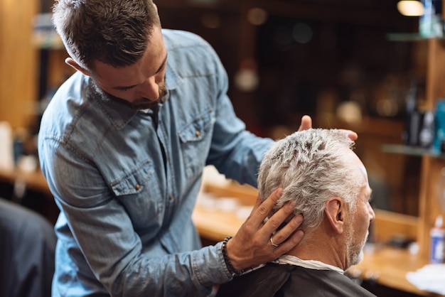 Masaje de cabeza. Vista posterior del cliente senior de peluquería obteniendo su cabello peinado por un estilista profesional.