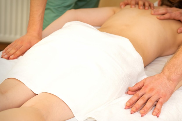 Masaje doble de espalda y manos a cuatro manos de dos masajeadores profesionales para una joven caucásica en un salón de spa.